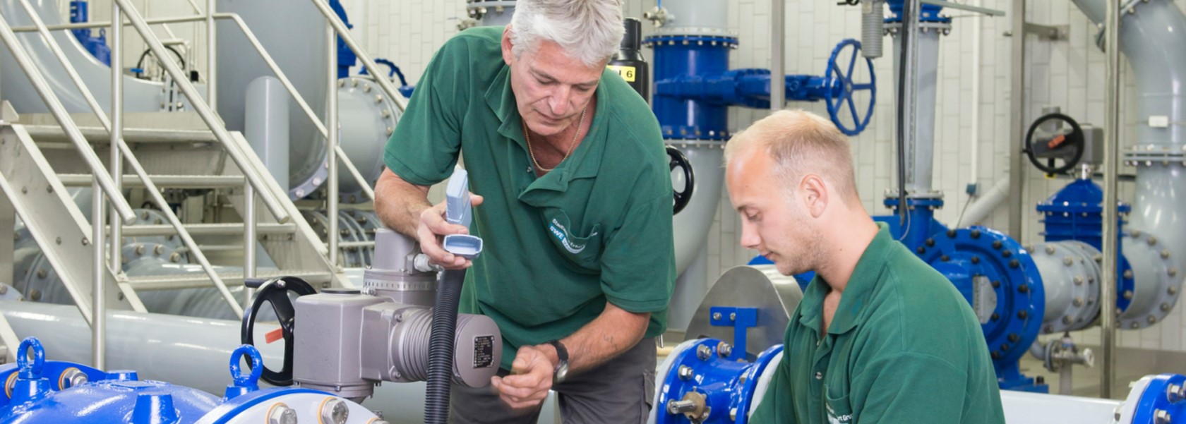 Zwei Techniker in grünen T-Shirts beim Prüfen einer Wasserleitung.